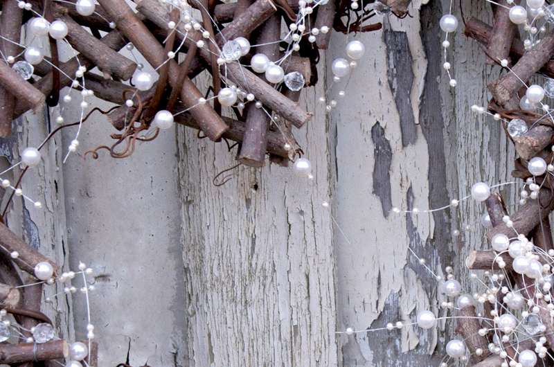 Heart shaped wreath made of twigs and decorated with pearls attached to a fence panel outside.