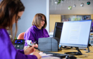 Two Fizzco employees in Fizzco's head office sat next to each other working at their desks.