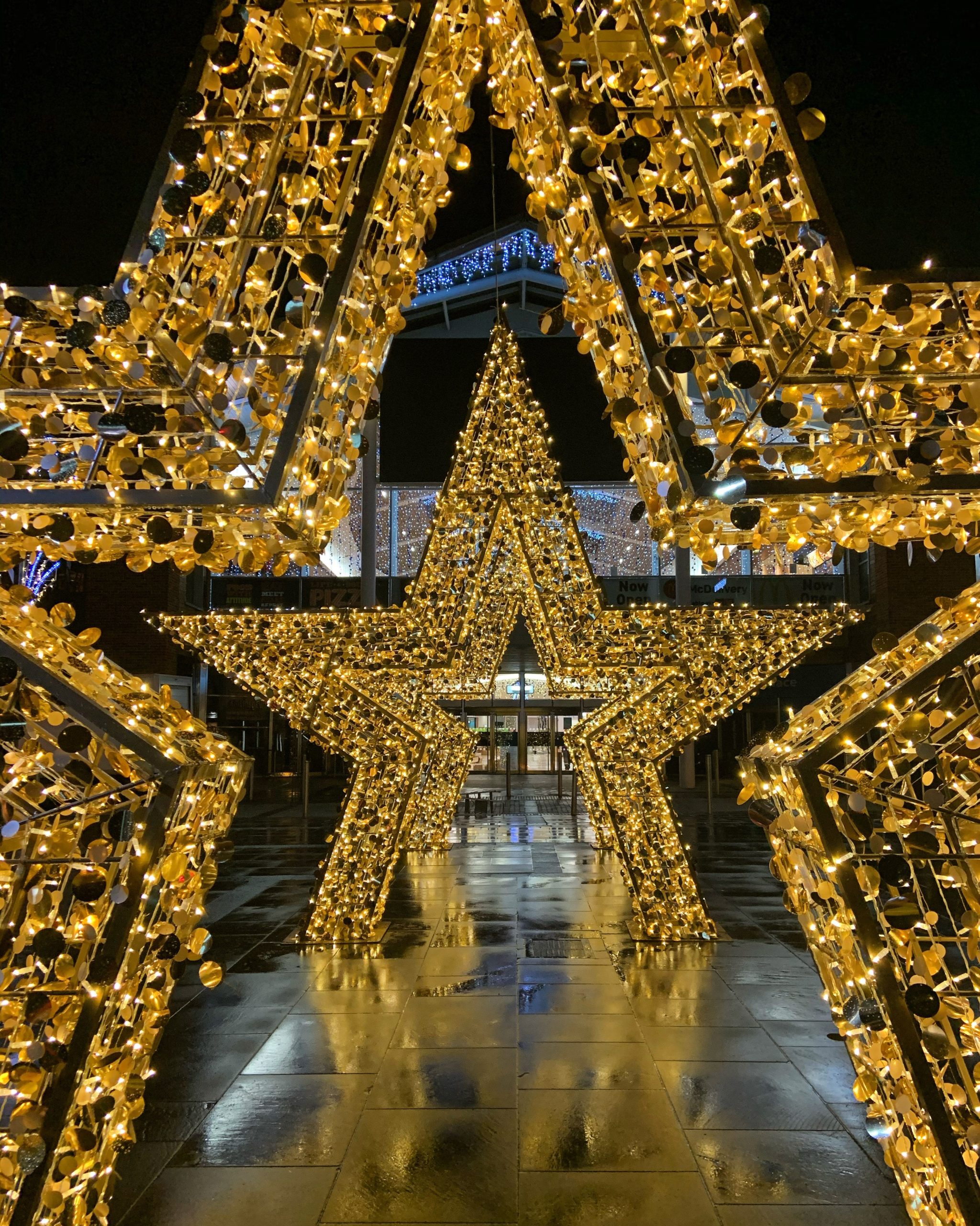 Three Light-up Gold Star Motifs displayed as a selfie point outside a shopping centre Christmas display.