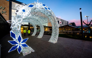 Bright white light up cylinder walkthrough tunnel decorated with silver tinsel and white and blue snowflakes leading to the entrance of Telford Shopping Centre.