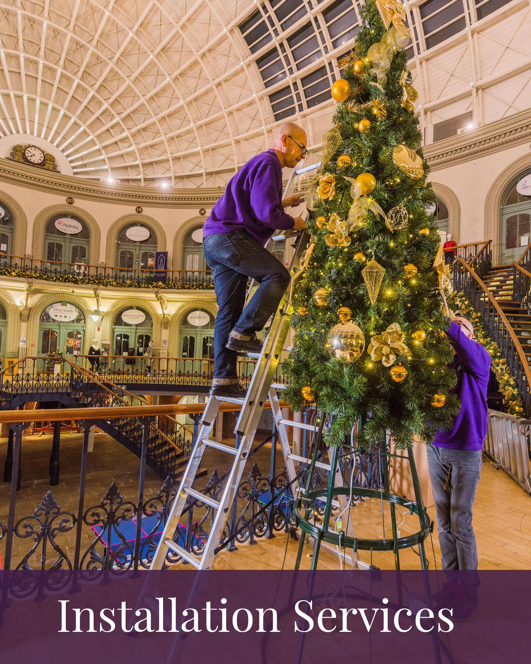 Icon with the words 'Installation Services' at the bottom and image of Two members of Fizzco's installation team installing an artificial cone Christmas tree decorated with gold baubles at Leeds Corn Exchange.