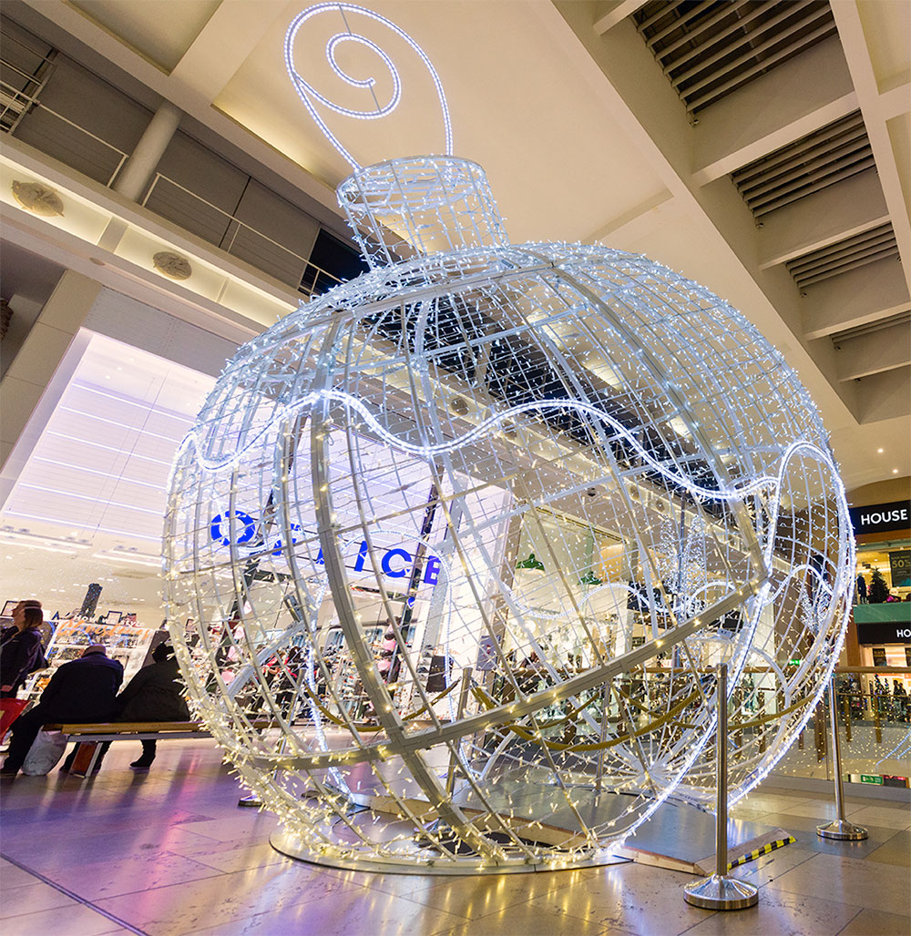 A 3D bauble motif in bright white and warm white lights displayed in the middle of a shopping centre.