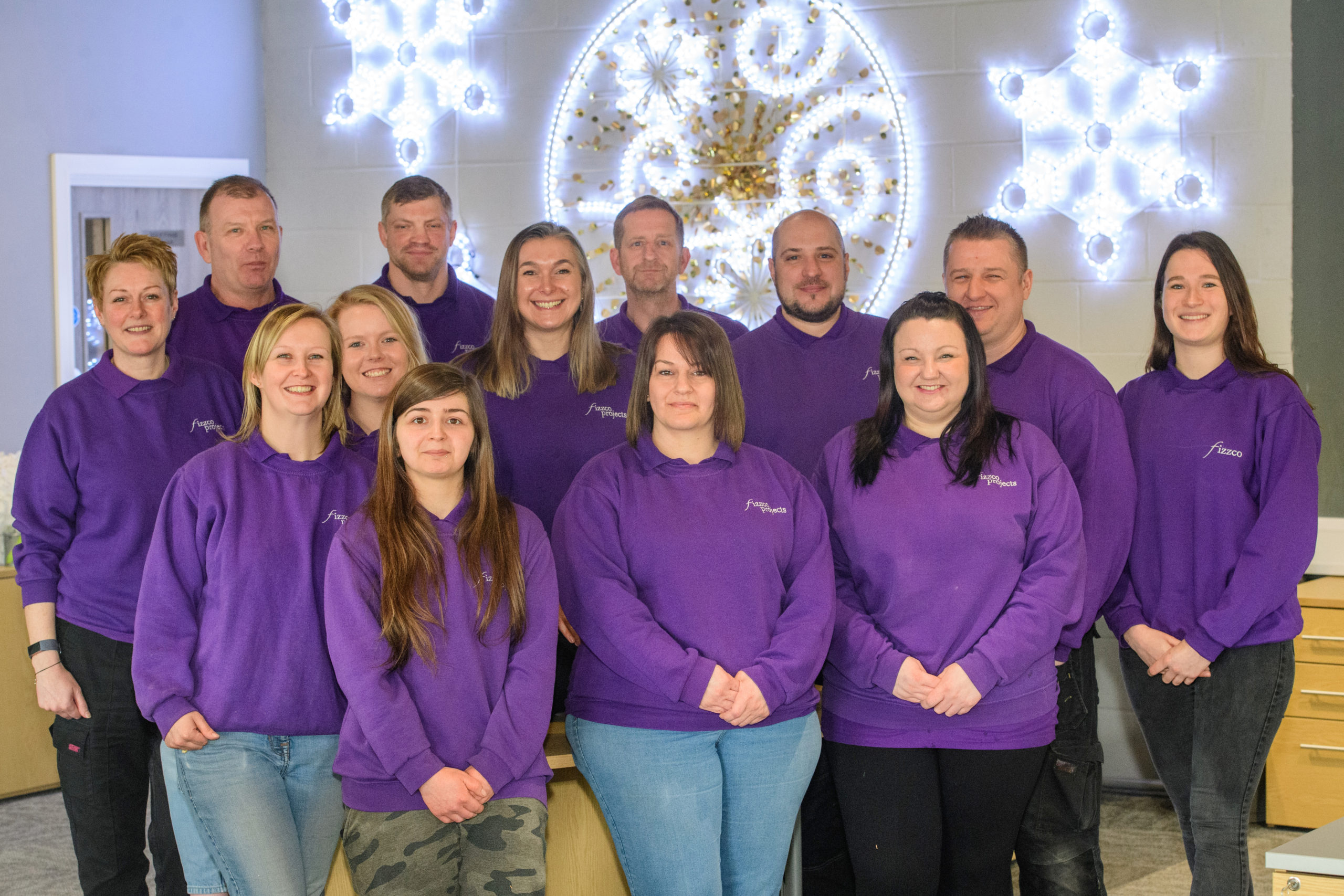 A whole team photo of Fizzco staff members wearing Fizzco's purple uniform in the head office.