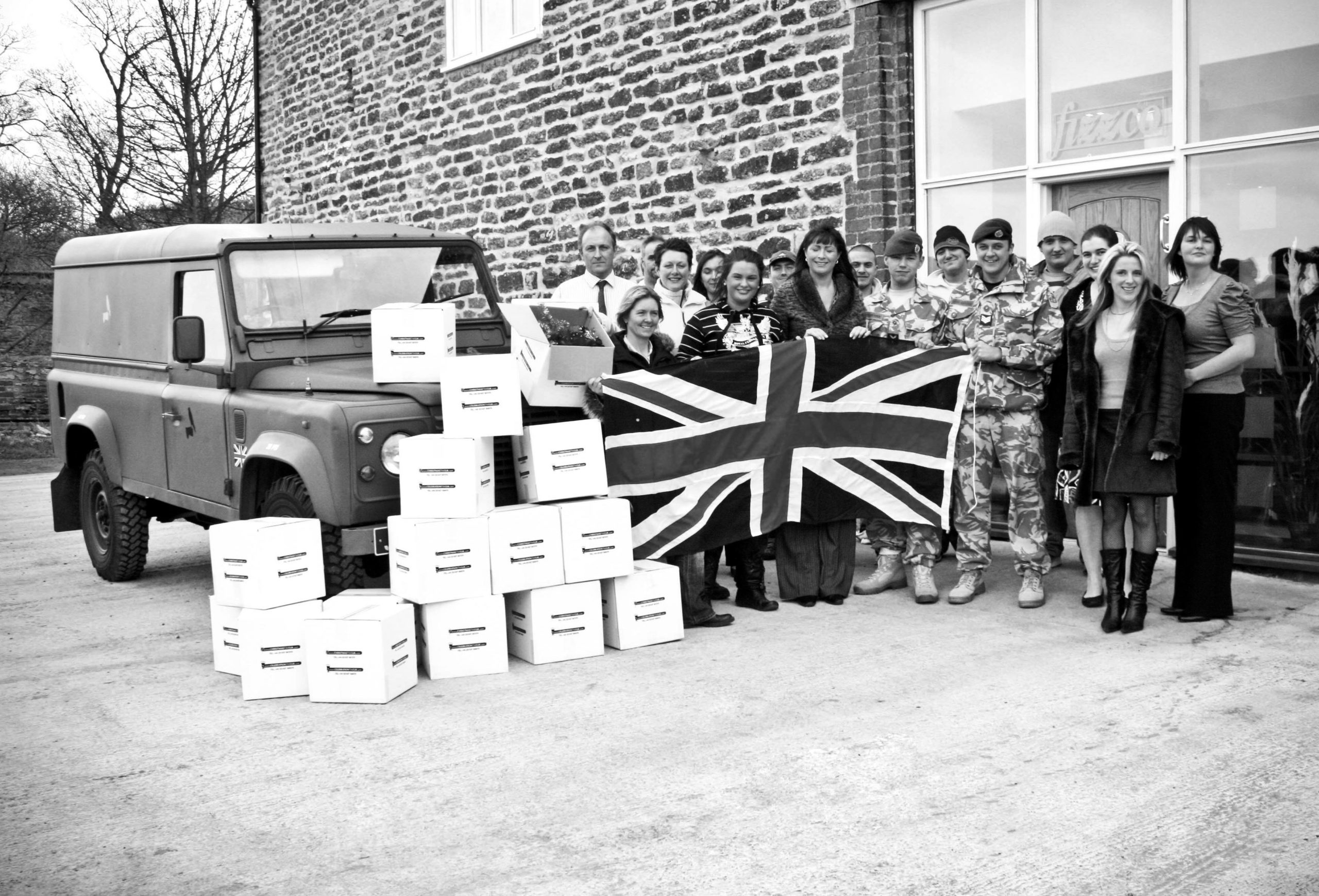 Black and white image of Fizzco staff members stood outside Fizzco, holding a union jack flag.