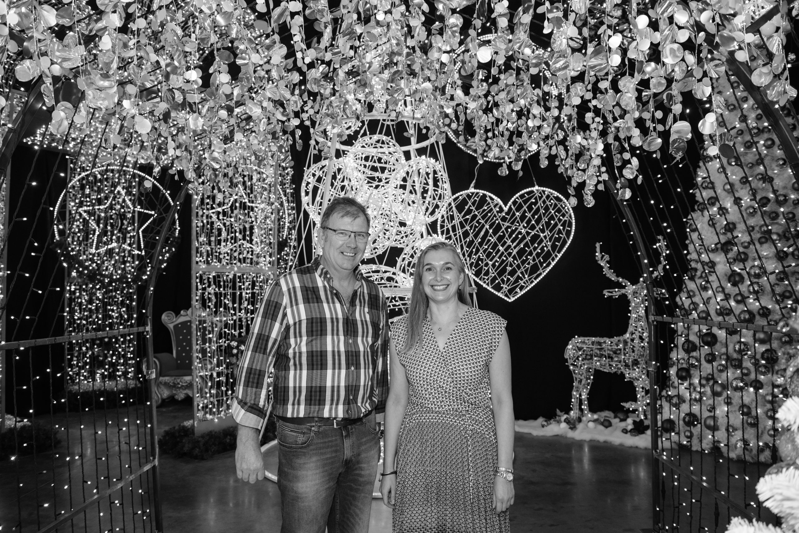 Black and white image of Fizzco's two directors stood underneath a light up arch with Christmas display products in the background for the official launch of the new Fizzco Christmas showroom.