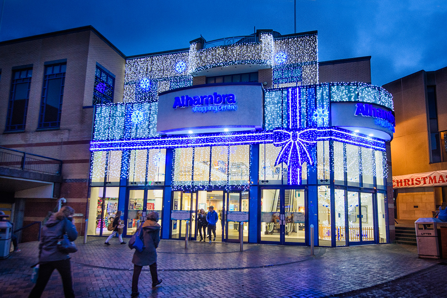 Light up blue ribbon bow with bright white curtain lights and bright white snowflake motifs on the outside wall of Alhambra Shopping Centre.