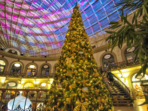 A large scale artificial green cone Christmas tree decorated with gold baubles, fauna, stars and bows at Leeds Corn Exchange.