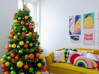 An artificial green Christmas tree decorated with yellow, orange and green baubles.