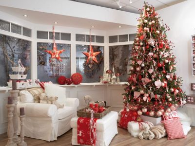 A Christmas display featuring an artificial green Christmas tree decorated with red and white decorations placed by a window with two red stars hanging in from of it.