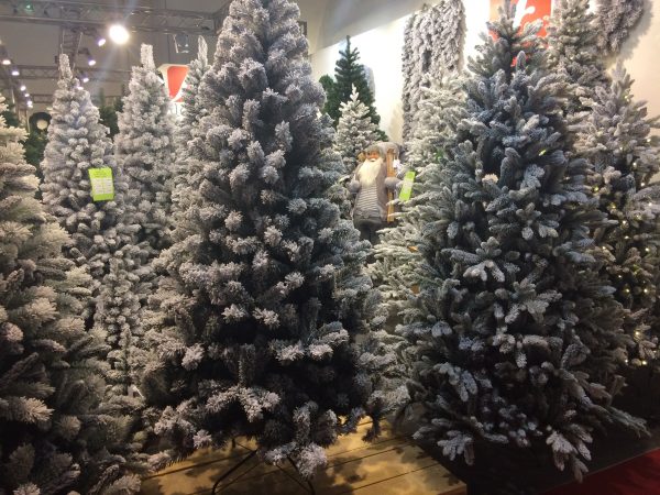 A display of several plain flocked green Christmas trees together inside a warehouse.