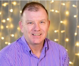 A headshot image of a Fizzco director in front of warm white curtain lights.