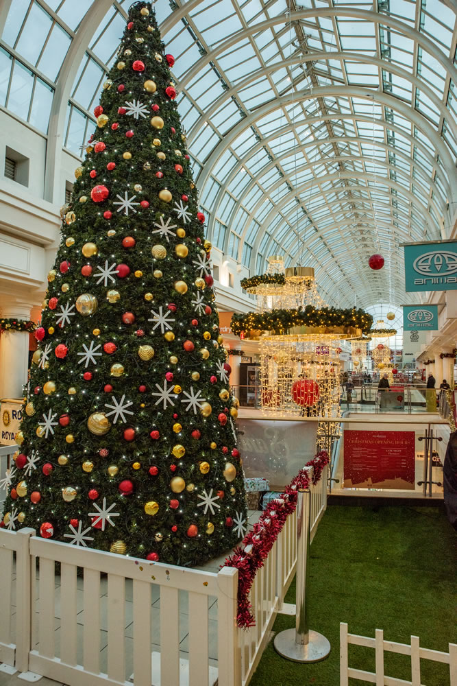 A traditional Christmas display at a shopping Centre featuring a large scale artificial cone Christmas Tree, Garlands and Chandeliers, with red and gold baubles and warm white lights.