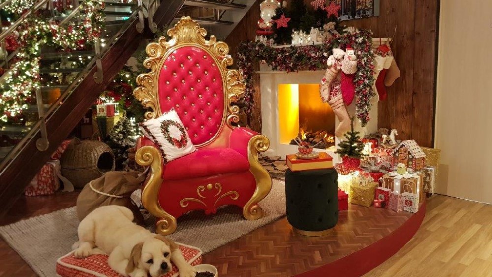 A Christmas display featuring a red and gold chair, a fireplace with a garland and stockings attached to it, and gifts next to the fireplace.
