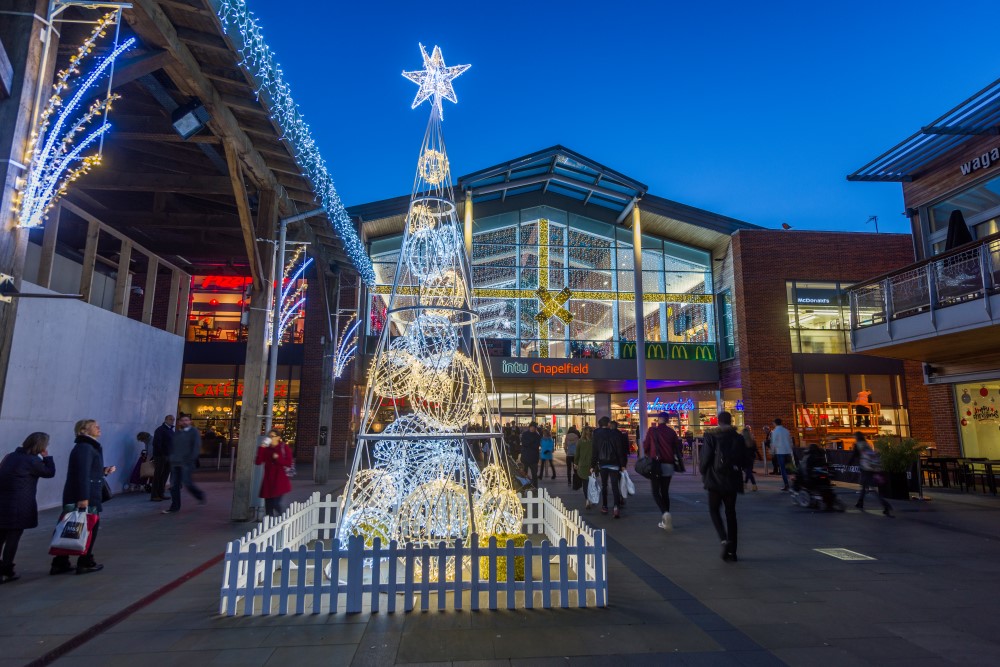 A contemporary light up Christmas tree outside Chapelfield Shopping Centre with warm white and bright white aurora balls stacked within the frame, and a gold star on top.