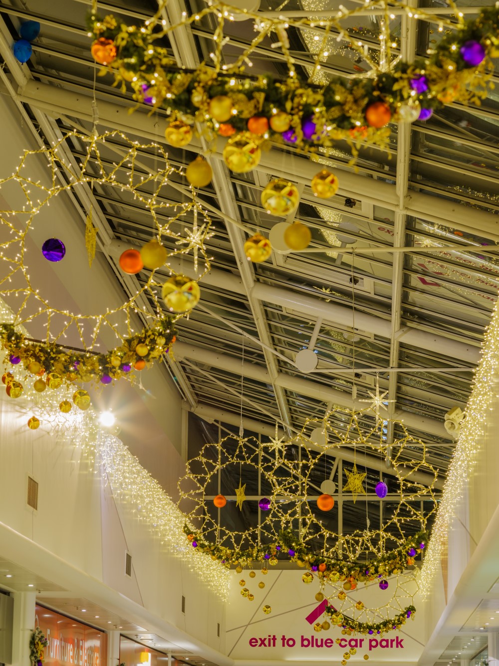 Warm white light up silhouettes suspended from the ceiling with green garlands attached to them decorated with gold, copper and purple baubles.