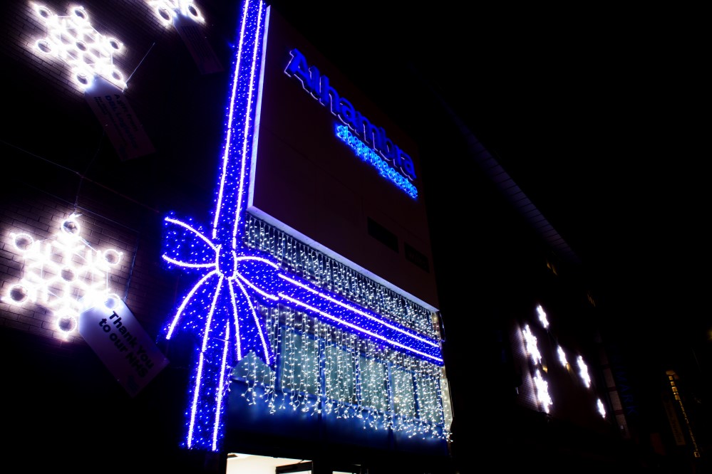 Light up blue ribbon bow with bright white curtain lights and bright white snowflake motifs on the outside wall of Alhambra Shopping Centre.