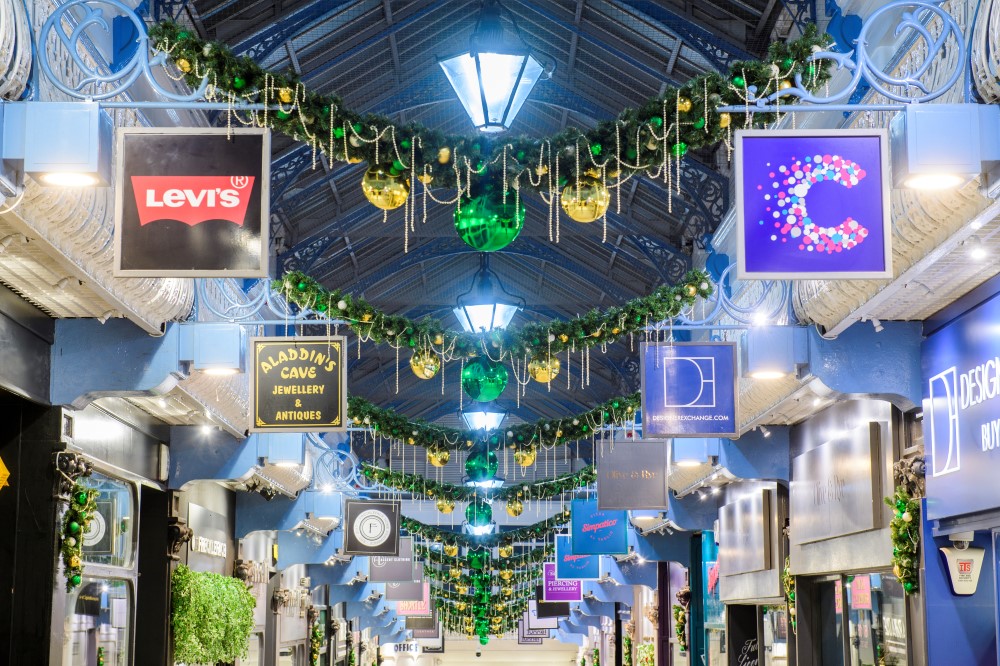 A row of garlands decorated with gold and green baubles and gold beads, suspending from the ceiling above the walkway in Queens Arcade Shopping Centre.