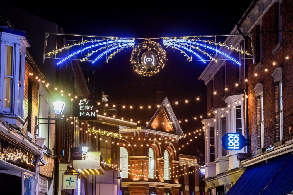 Christmas lights displayed outside in the Cornhill Quarter in lincoln, featuring bright white and warm white lights either side of the CQ sign, and warm white festoon lights zigzagged above the footpath.