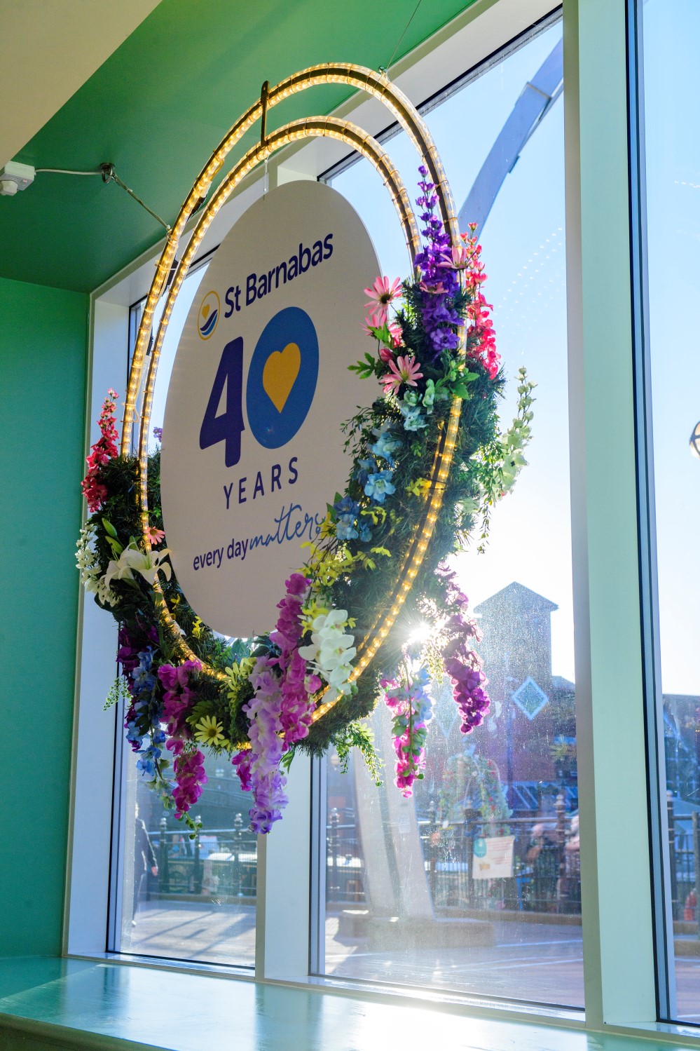 Light up floral wreath with purple, pink, blue, yellow, green, and white flowers around St Barnabas 40 year anniversary sign in the Waterside Shopping Centre, Lincoln.