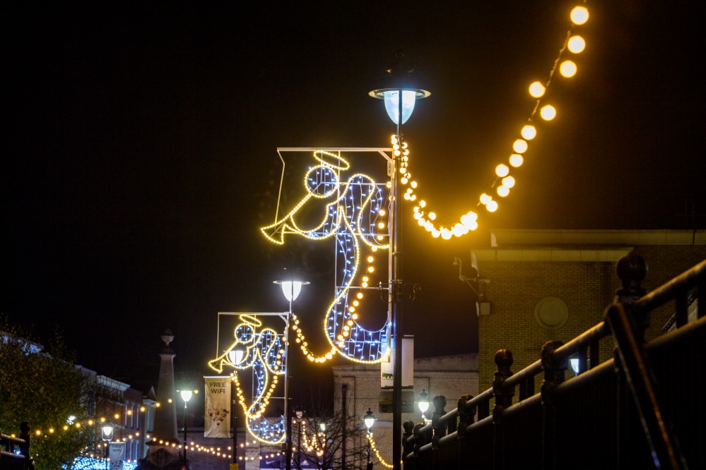 Two angel motif lights blowing trumpets in bright white colour with a warm white outline, attached to street lights.