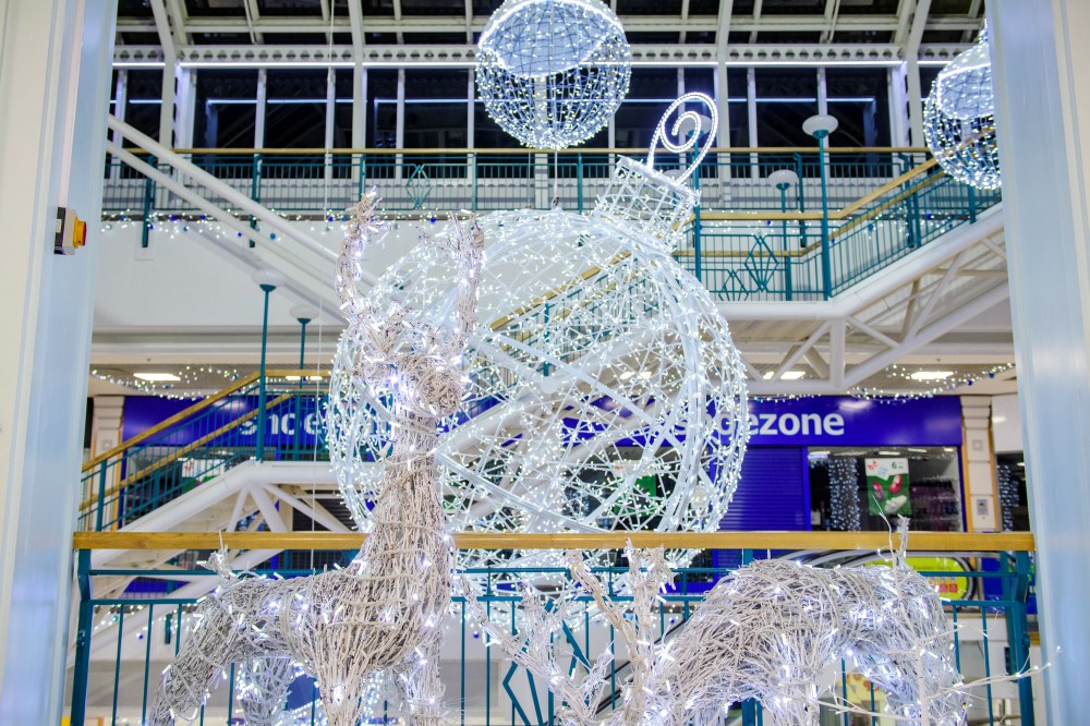 A Christmas display at Alhambra shopping centre featuring a large bright white bauble motif on the ground with two smaller white bauble motifs suspended from the ceiling above it, and two white light up reindeers at the front.