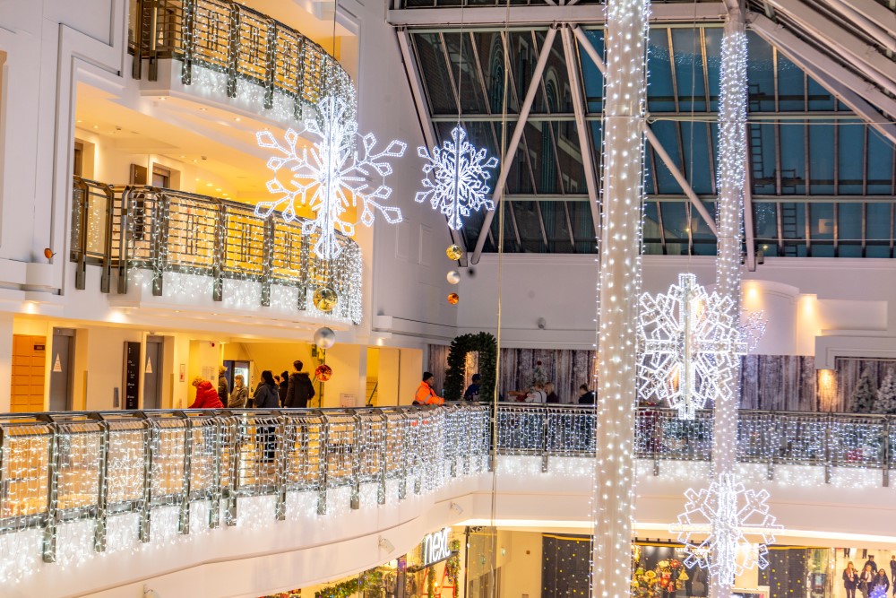 Bright white snowflake motifs suspended from the ceiling and bright white curtain lights wrapped around the pillars and the railings in the shopping centre.