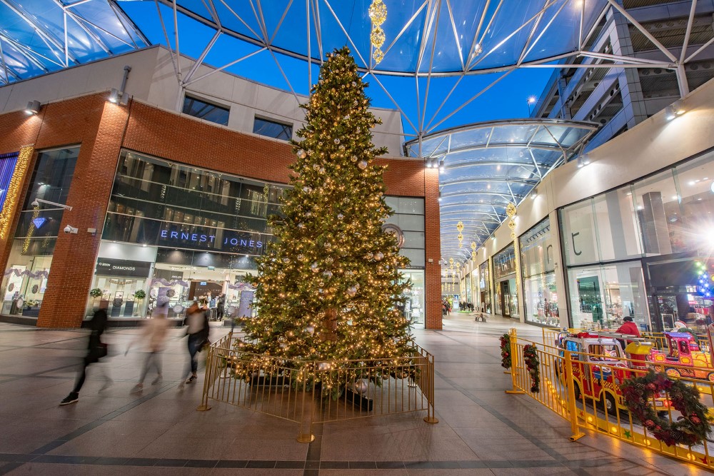 Large scale artificial Christmas Tree decorated with gold and silver baubles standing in the centre of a shopping centre.