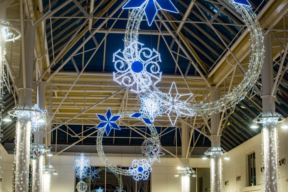 A Winter Wonderland Christmas display featuring bright white circular motifs suspended from the ceiling, decorated with blue and white snowflakes, and white and blue snowflakes suspended from the ceiling, with bright white curtain lights around the pillars.