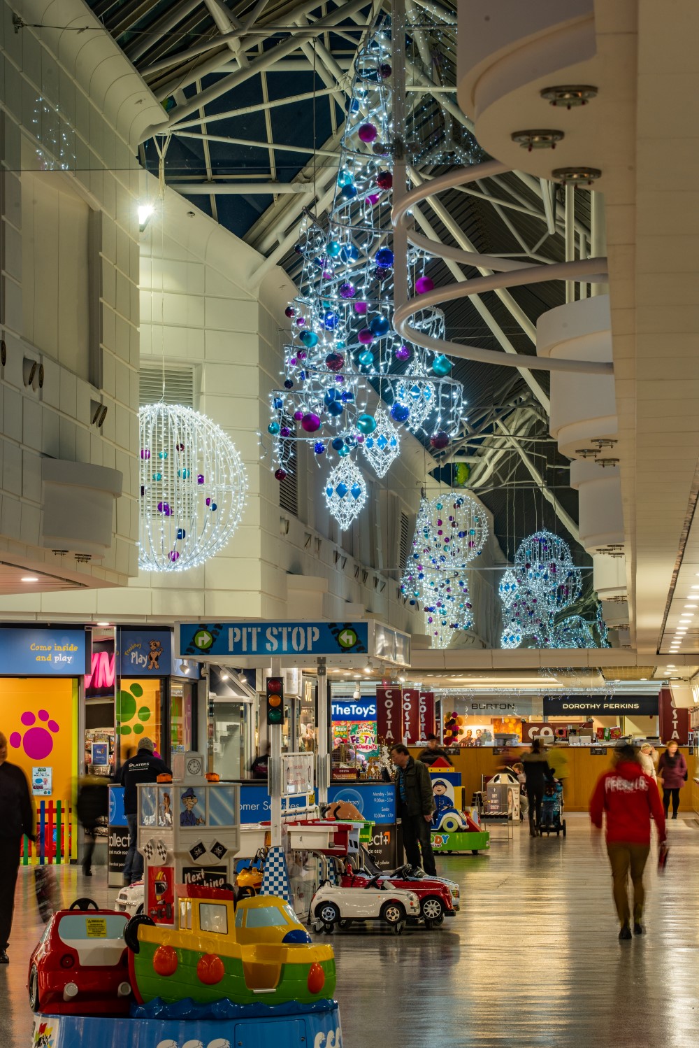 Large bright white aurora balls and spiral Christmas trees suspended from the ceiling, decorated with light blue, dark blue and purple baubles.