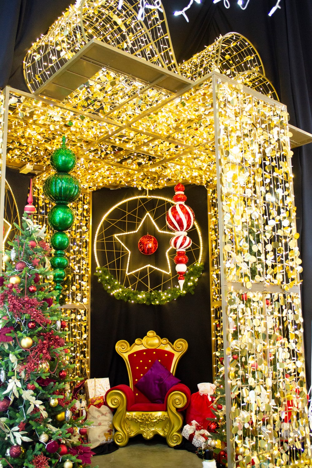 Christmas scene display designed by Fizzco Projects featuring a light up gold 3D present Motif with a gold and red throne, gift, a large green hanging decoration, a large red and white striped hanging decoration and a 2D light up star motif.