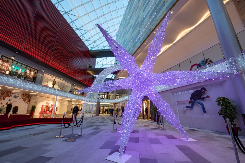 A shopping centre Christmas display featuring a large light up colour changing shooting star and bright white icicle lights around the wall of the centre of the Shopping Centre.
