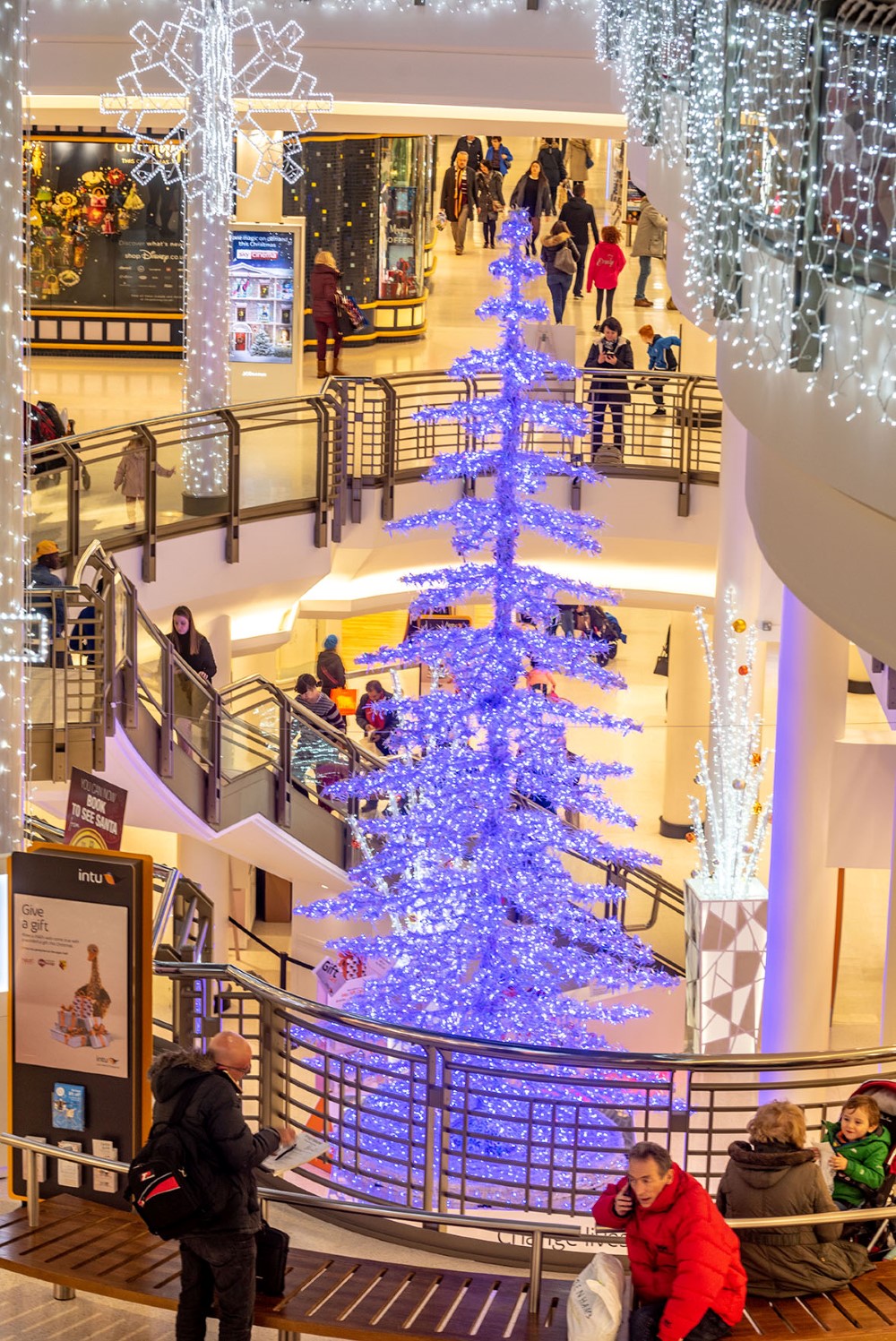 Large-scale light up colour changing artificial Christmas Tree placed in the centre of the Shopping Centre, surrounded by Bright White Curtain Lights and a 3D Snowflake Motif. as part of a Christmas display.
