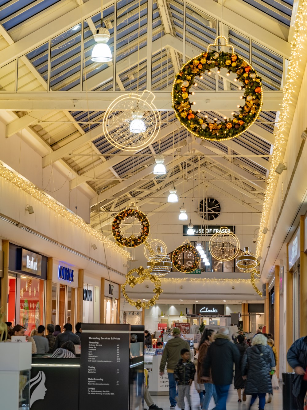 A shopping centre display featuring bauble motifs suspended from the ceiling in warm white and warm white and green decorated with gold and copper baubles.