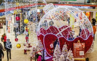 Shopping Centre Christmas Grotto featuring red and white light-up bauble motif with white Christmas trees and curtain light chandeliers with red, gold, and silver baubles.