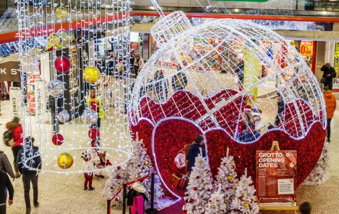 Shopping Centre Christmas Grotto featuring red and white light-up bauble motif with white Christmas trees and curtain light chandeliers with red, gold, and silver baubles.