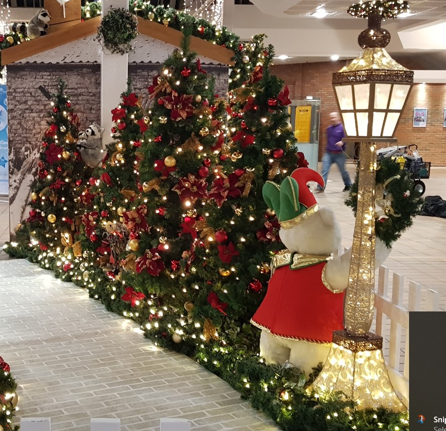 A Christmas Grotto display featuring a white wooden grotto, a gold light up street light and four artificial Christmas trees with red and gold baubles and flowers.