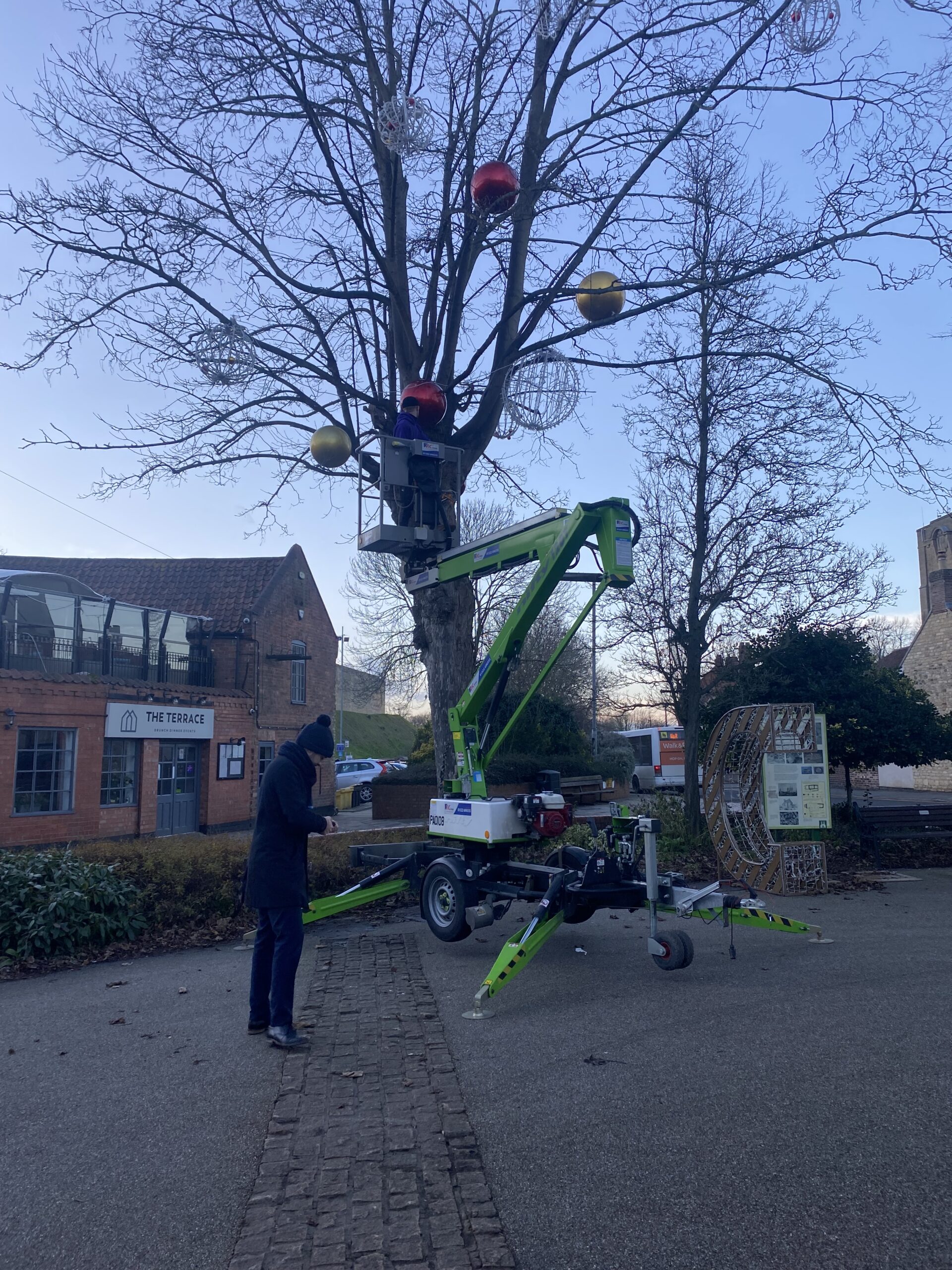 A member of Fizzco's installation team in a scissor lift uninstalling the light up Aurora Balls from a tree in Lincoln's Christmas display.