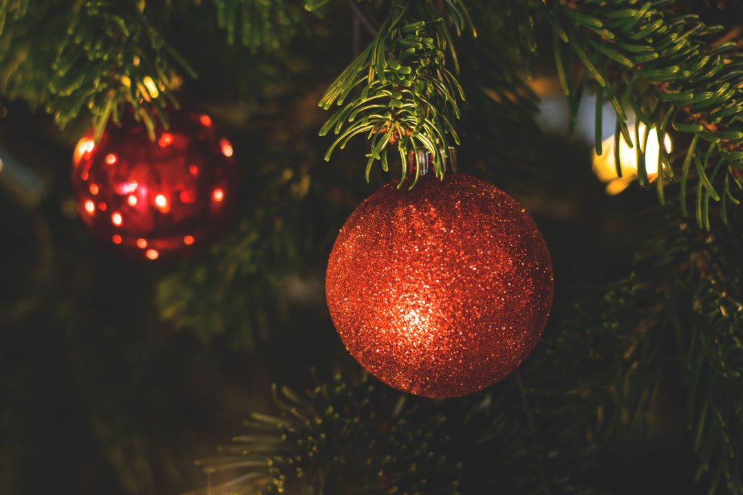 Close up image of Christmas decorations on a green Christmas tree featuring red baubles